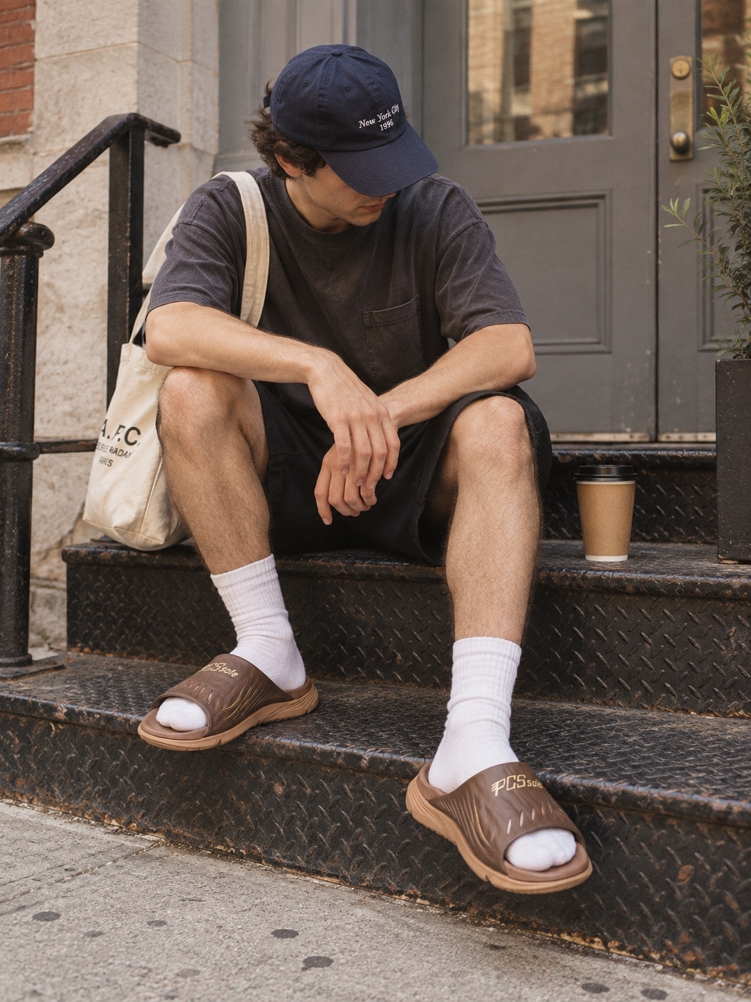 A man sits on black diamond-plate outdoor steps wearing brown slide sandals with white socks