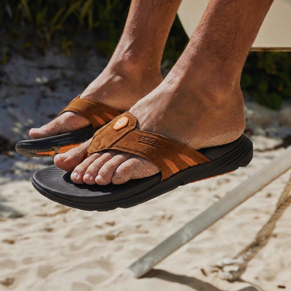 Close-up of a man's feet wearing PCSsole Mocha Suede arch support flip flops on the beach