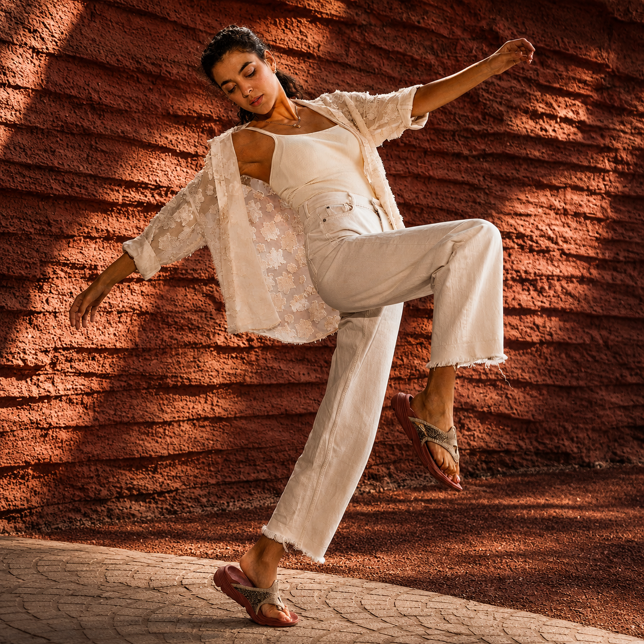 Dancer in a flowing white outfit against a textured red-brown wall.